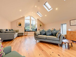 A spacious loft-style room with a high ceiling, a large window offering a view of the outdoors, a built-in bench, and a wooden cabinet. - 3 Bed in Keswick (oc-93589) (Threlkeld)