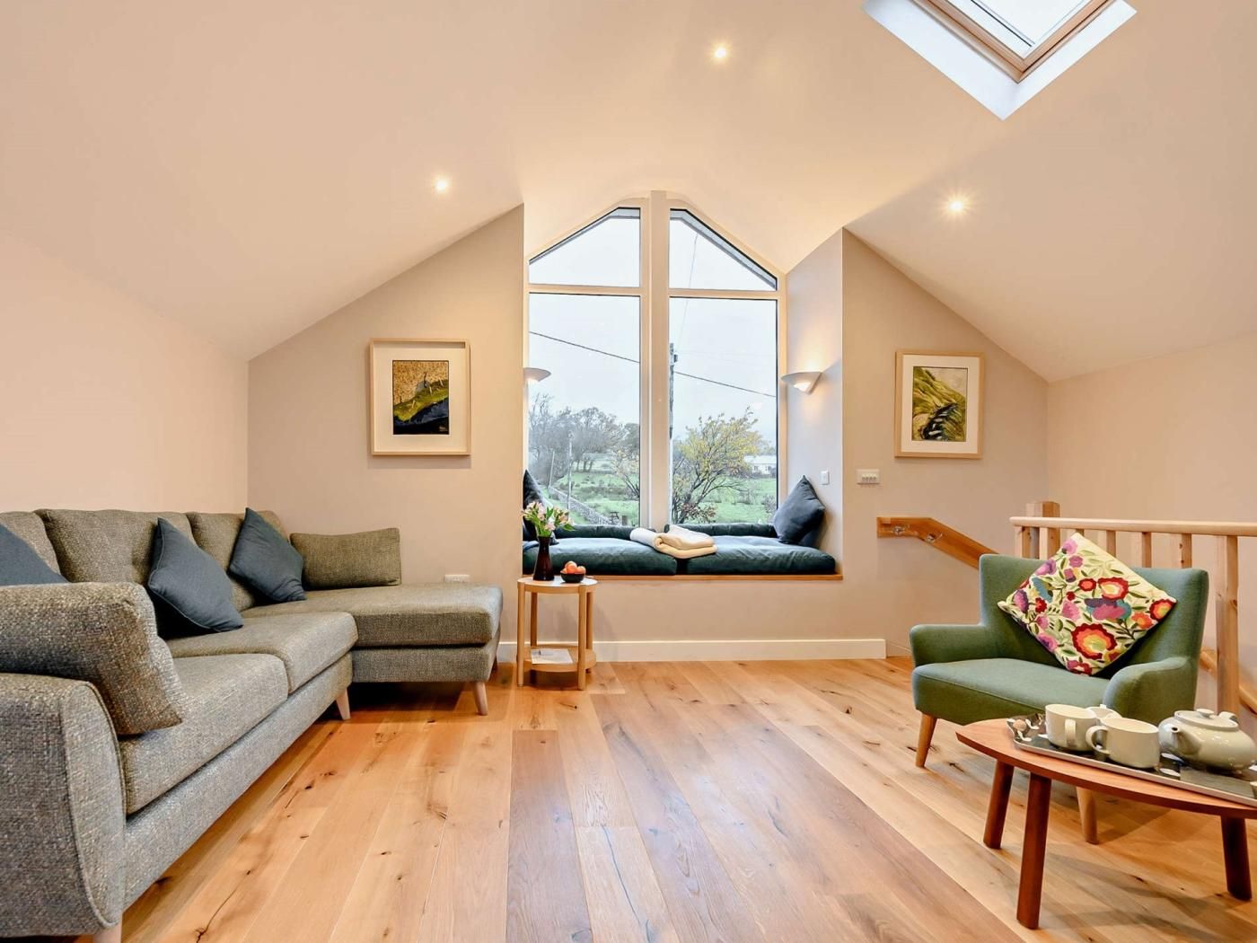 A cozy loft bedroom with a large skylight, a green sofa, a wooden coffee table, and a view of the outdoors.