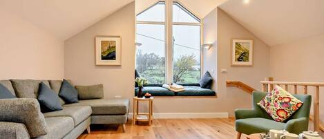 A cozy loft bedroom with a large skylight, a green sofa, a wooden coffee table, and a view of the outdoors.