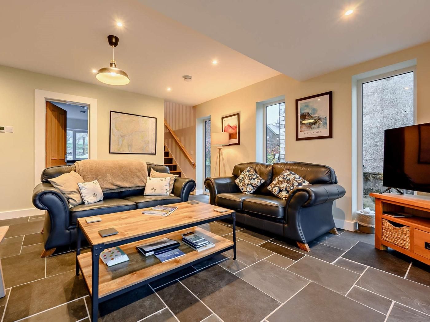 A modern living room with two leather sofas, a wooden coffee table, and a television on a wooden stand.