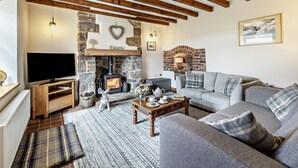A cozy living room with a stone fireplace, wooden beams, a sofa, and a television. - 2 Bed in Llandudno Junction (oc-93622) (Bryn Pydew)