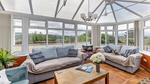 A conservatory with a high ceiling, large windows, and a view of the countryside. - 2 Bed in Llandudno Junction (oc-93622) (Bryn Pydew)