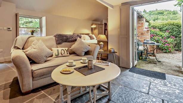 Ein gemütliches Wohnzimmer mit einer Couch, einem kleinen Tisch mit einer Essschale und einem Fenster mit Blick auf Grünflächen.