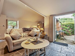Ein gemütliches Wohnzimmer mit einer Couch, einem kleinen Tisch mit einer Essschale und einem Fenster mit Blick auf Grünflächen.
