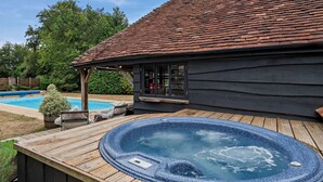 Ein Whirlpool auf einer Holzterrasse, ein Schwimmbecken und ein Haus mit schrägem Dach.