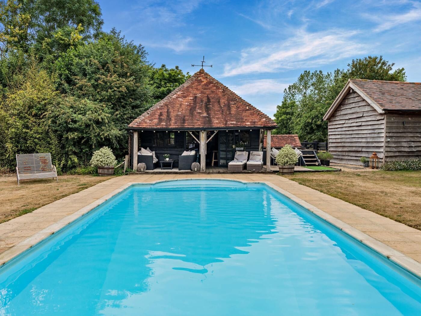 A swimming pool with a covered seating area and a wooden building in the background.