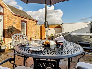 Eine Terrasse mit einem runden Metalltisch, Stühlen, einem Grill und einem Backsteinhaus im Hintergrund.