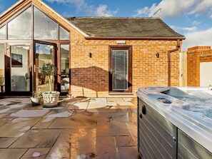 Een bakstenen huis met een glazen deur, een hottub en een terras met stenen tegels.