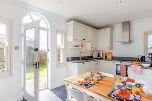 Eine moderne Küche mit weißen Schränken, einem für das Frühstück gedeckten Esstisch und Blick durch eine Glastür.