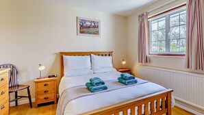 A bedroom with a wooden bed, two bedside tables, a chair, a window with curtains, and a painting on the wall. - 2 Bed in Bembridge (oc-ic042) (Bembridge)