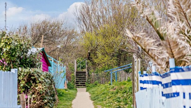 A pathway leading to a gated entrance with a staircase, surrounded by greenery and fences. - 2 Bed in Bembridge (oc-ic042) (Bembridge)