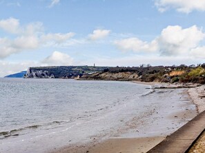A coastal landscape with a sandy beach, a cliff, and a distant hill. - 2 Bed in Bembridge (oc-ic042) (Bembridge)