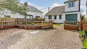 A residential property with a paved driveway, wooden fences, and a garage. - 2 Bed in Bembridge (oc-ic042) (Bembridge)
