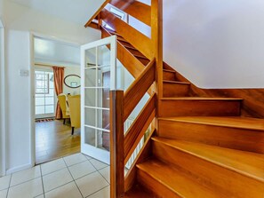 Un escalier en bois mène à une pièce qui contient une porte, une chaise et une fenêtre.