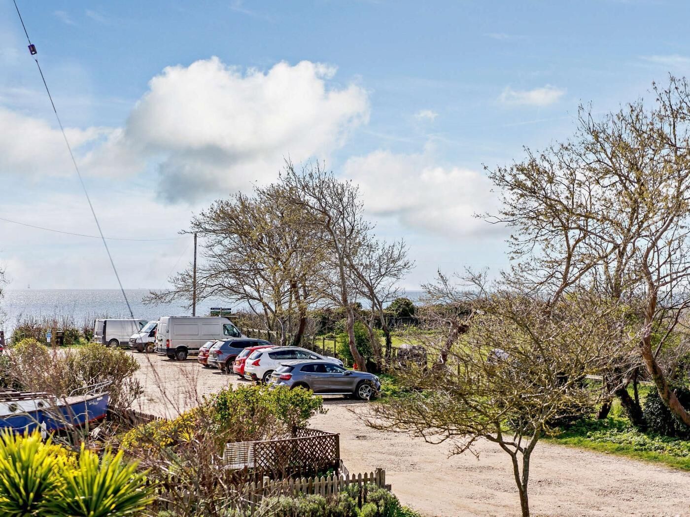 A parking area with vehicles, a boat, and a view of the sea.