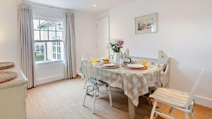 Un comedor con una mesa dispuesta para dos personas, una ventana con cortinas, un radiador y un cuadro en la pared.
