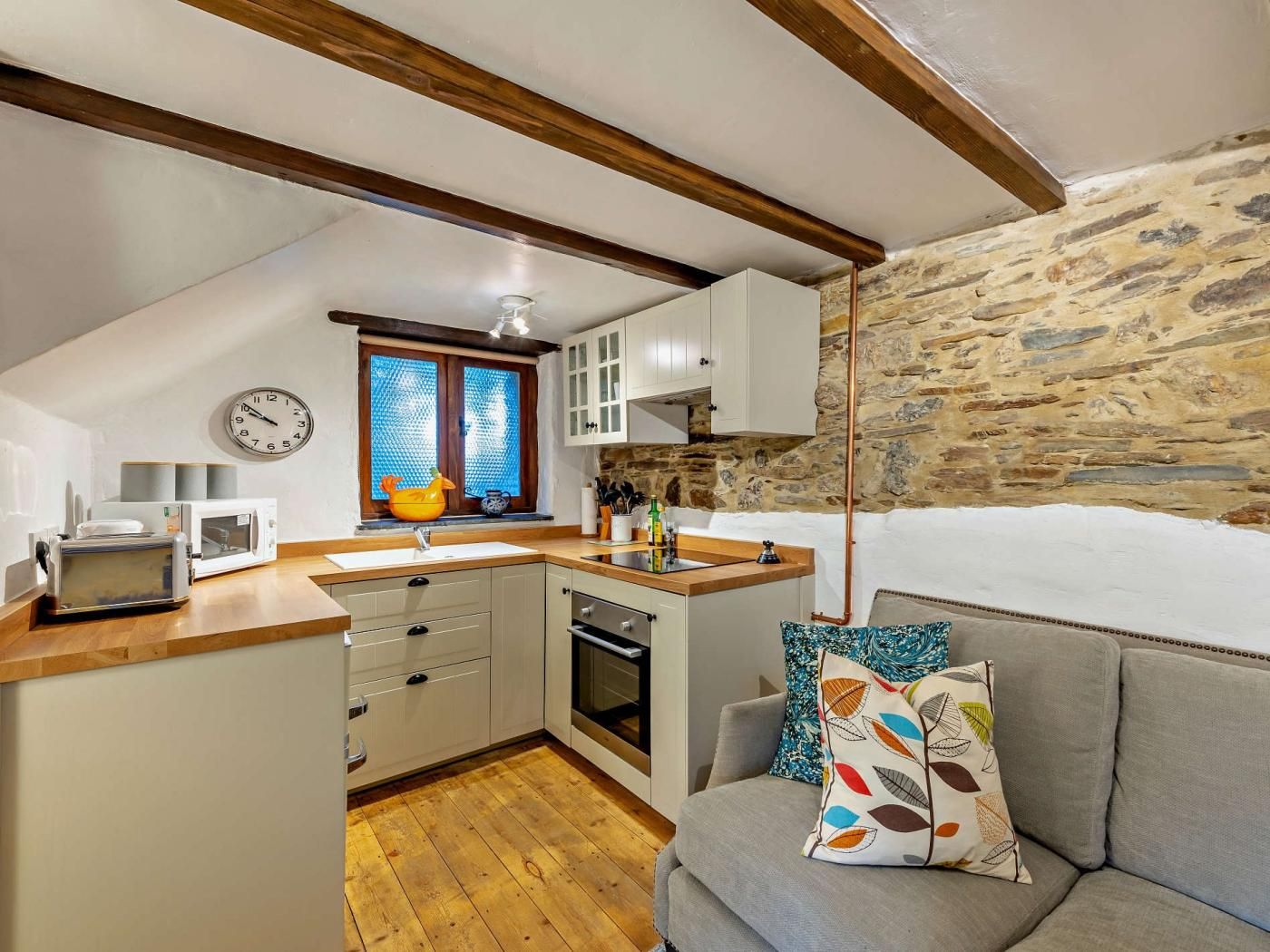 A compact kitchen with a wooden countertop, a built-in oven, and a stone wall.