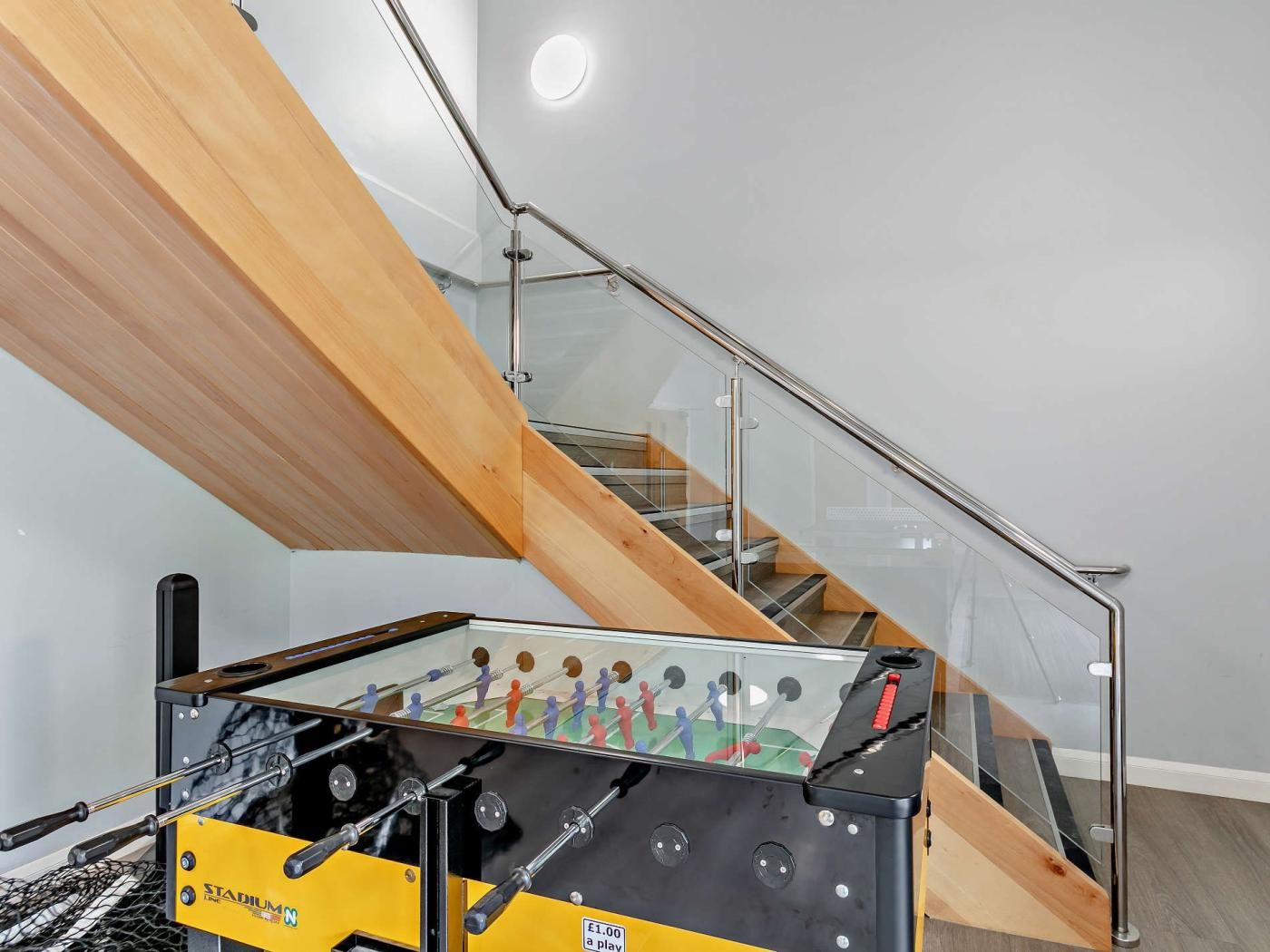 Un espace intérieur moderne doté d’un escalier en verre, d’une table de baby-foot et d’une structure de plafond en bois.