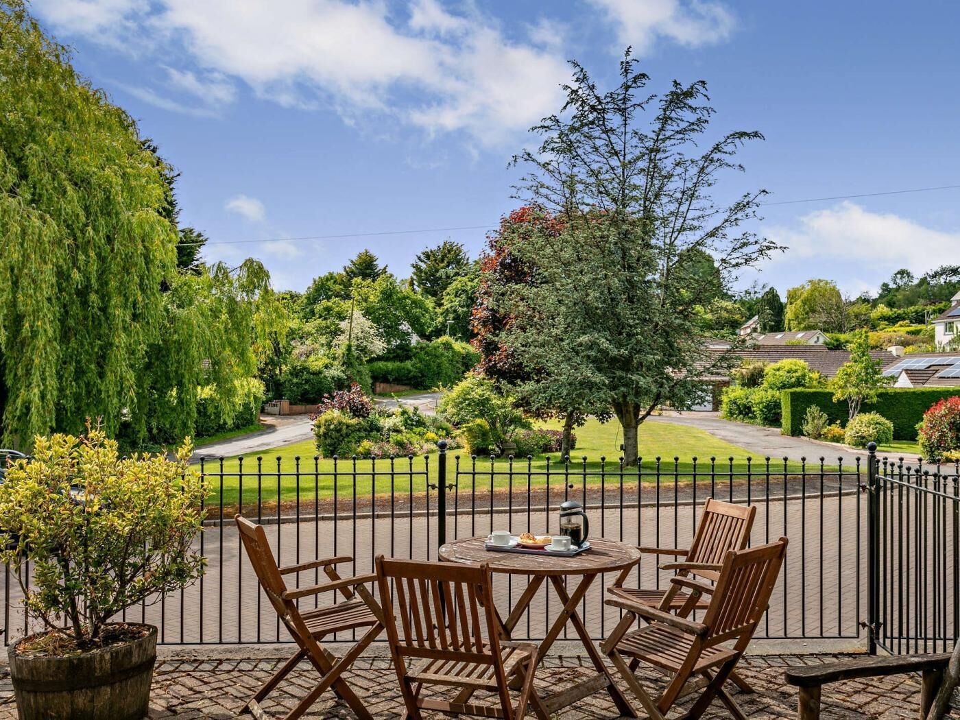 A patio with a round table and four chairs, overlooking a well-maintained garden and a residential street.