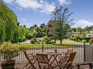 Eine Terrasse mit einem runden Tisch und vier Stühlen mit Blick auf einen gepflegten Garten und eine Wohnstraße.