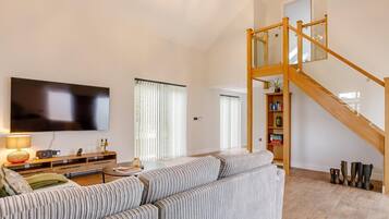 A living room with a large flat-screen TV, a sofa, a coffee table, and a staircase.