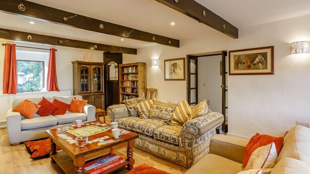 Una sala de estar con un sofá, un sillón estampado, una mesa de centro de madera con juegos de mesa, una estantería y una puerta que da a otra habitación.
