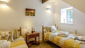 Un dormitorio con dos camas individuales, una mesita de noche con lámpara, un cuadro y una ventana con vistas a zonas verdes.
