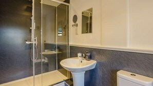 Un baño moderno con ducha de vidrio, lavamanos pedestal y retrete.