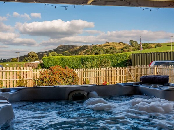 A hot tub with a wooden fence and a view of a hill.