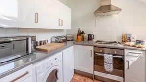 A compact kitchen with a washing machine, a toaster, a kettle, and a stove. - 2 Bed in Appledore (oc-gable) (Appledore)