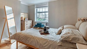 Een slaapkamer met een bed, een kaptafel, een raam en een spiegel.