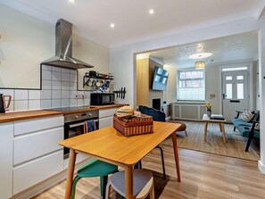 A compact kitchen with modern appliances, a dining area with a wooden table, and a living space with a sofa and TV.