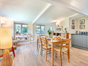 A dining area with a wooden table and chairs, a kitchen with grey cabinets, and a window with blinds. - 2 Bed in Brockenhurst (oc-94003) (Beaulieu)