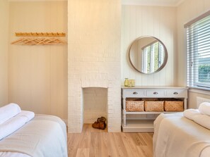 A bedroom with two beds, a white brick fireplace, a round mirror, and a window with blinds. - 2 Bed in Brockenhurst (oc-94003) (Beaulieu)