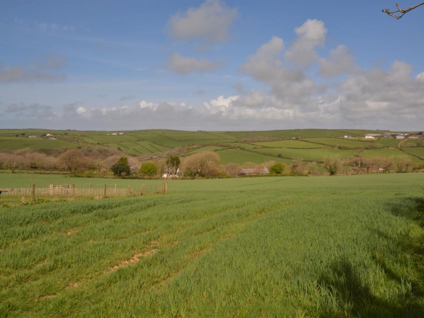 Un paysage rural caractérisé par des collines verdoyantes, une clôture en bois et des bâtiments dispersés.