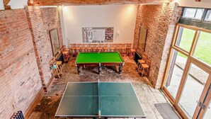 Une salle de billard équipée d’une table de billard, d’une table de ping-pong et de plusieurs chaises.