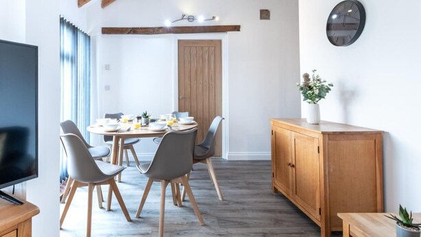 Un coin repas avec une table ronde, des chaises grises, des poutres en bois, un buffet en bois et une horloge au mur.