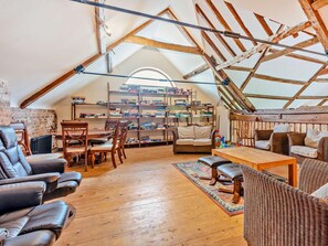 An attic room with a sloped ceiling, wooden beams, a bookshelf, leather chairs, a sofa, and a dining table. - 3 Bed in Doncaster (oc-93570) (Mattersey)