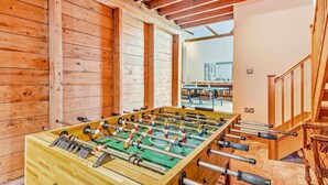 Ein Zimmer mit Holzboden, einer Tischfußballplatte, einer Treppe und Blick auf ein Gebäude.