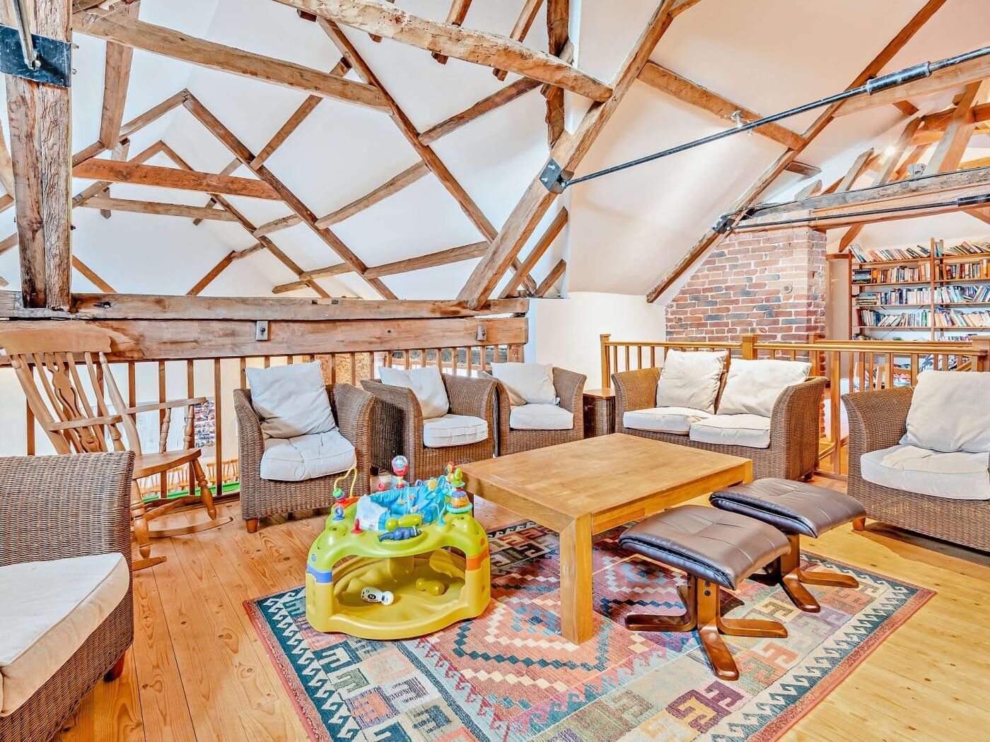 A cozy attic room with wooden beams, wicker furniture, a wooden table, and a bookshelf.