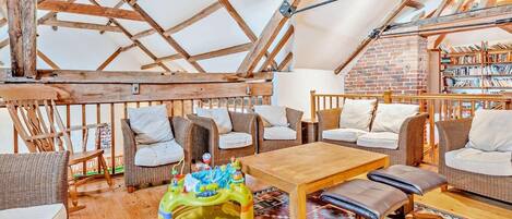 A cozy attic room with wooden beams, wicker furniture, a wooden table, and a bookshelf.
