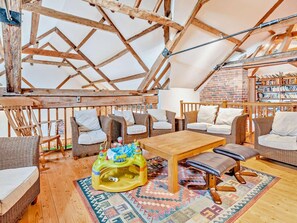 Ein gemütliches Dachzimmer mit Holzbalken, Korbmöbeln, einem Holztisch und einem Bücherregal.
