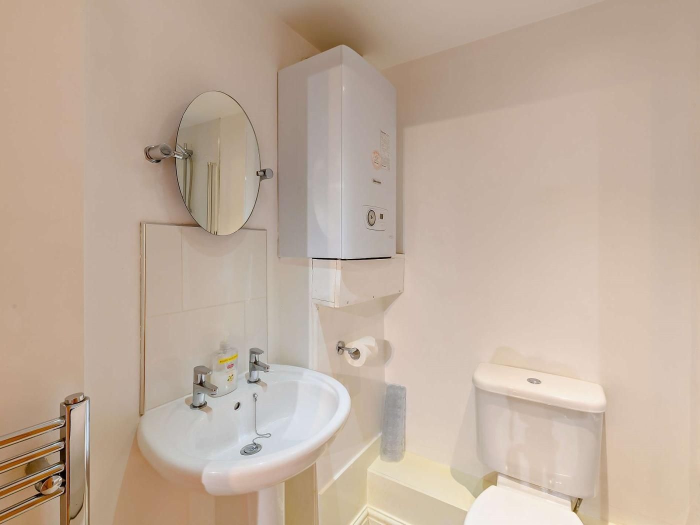Une salle de bain avec un lavabo blanc, un miroir, des toilettes et un meuble blanc placé au-dessus des toilettes.