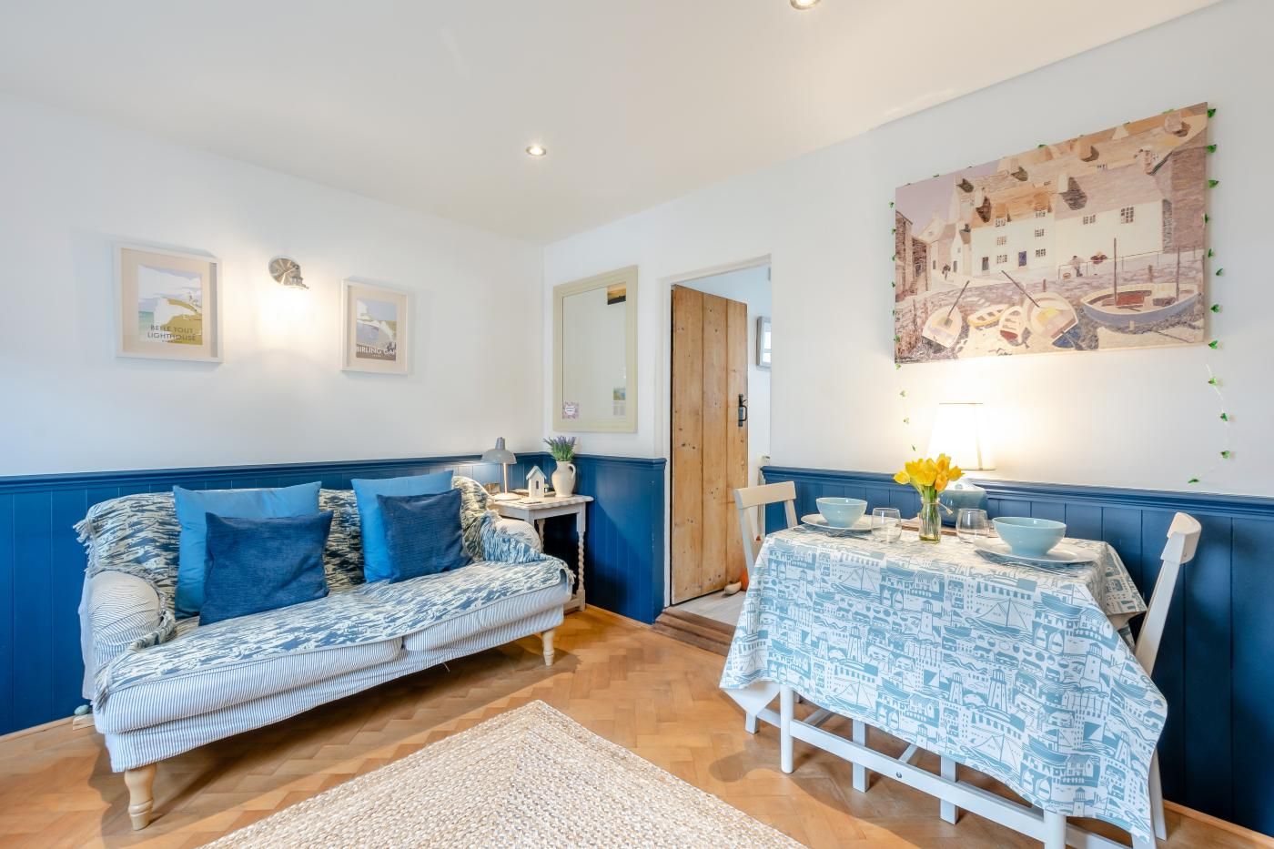 Ein Zimmer mit einem blau-weißen Sofabezug, einem Esstisch mit passender Tischdecke und einer Wand mit einem Stadtbild.