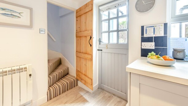 A kitchen with a wooden door, a clock, a framed fish illustration, and a bowl of fruit on the counter. - 1 Bed in Eastbourne (oc-ehc24) (Eastbourne)