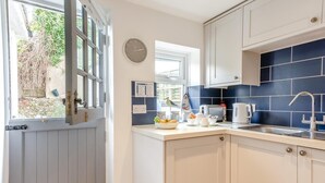 A kitchen with a window, a clock, and a blue tiled backsplash. - 1 Bed in Eastbourne (oc-ehc24) (Eastbourne)