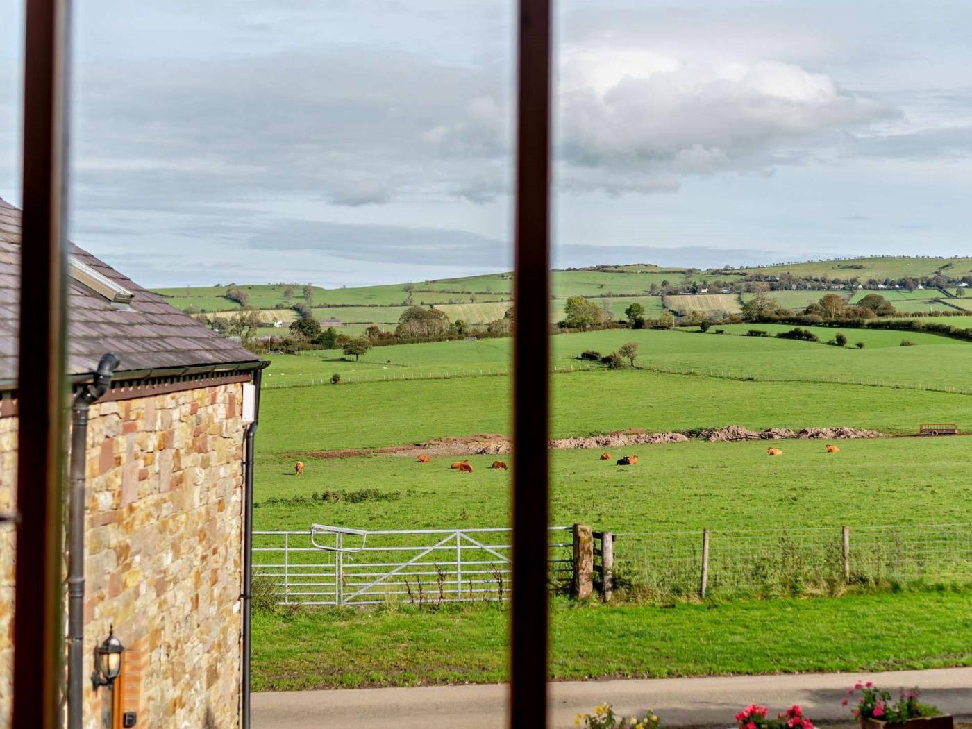 Un paysage rural avec un bâtiment en pierre, un portail en métal et un champ où paissent des vaches.