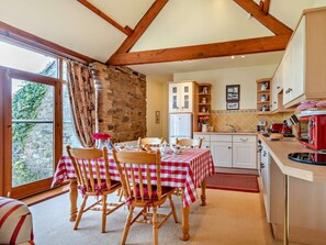 A cozy kitchen with a stone wall, wooden beams, a dining table with checkered tablecloths, and a red toaster. - 2 Bed in Wigton (oc-93463) (Ireby)