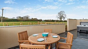 A round wooden table with chairs, a hot tub, and a view of a green field. - 2 Bed in Ripon (oc-94000) (Littlethorpe)