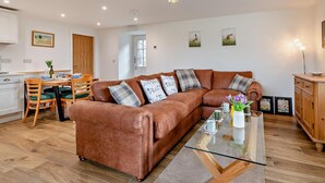 A living room with a brown leather sofa, a glass coffee table, and a dining area with wooden chairs and a white table. - 2 Bed in Ripon (oc-94000) (Littlethorpe)